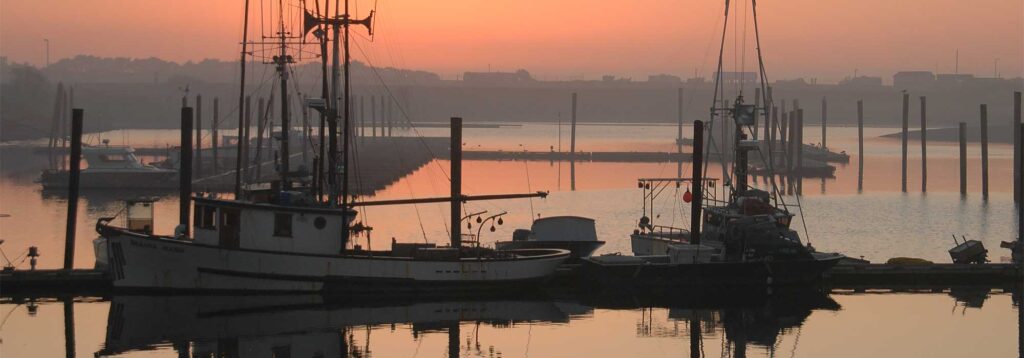 Peaceful coastal harbor town with boats and golden hour beach light